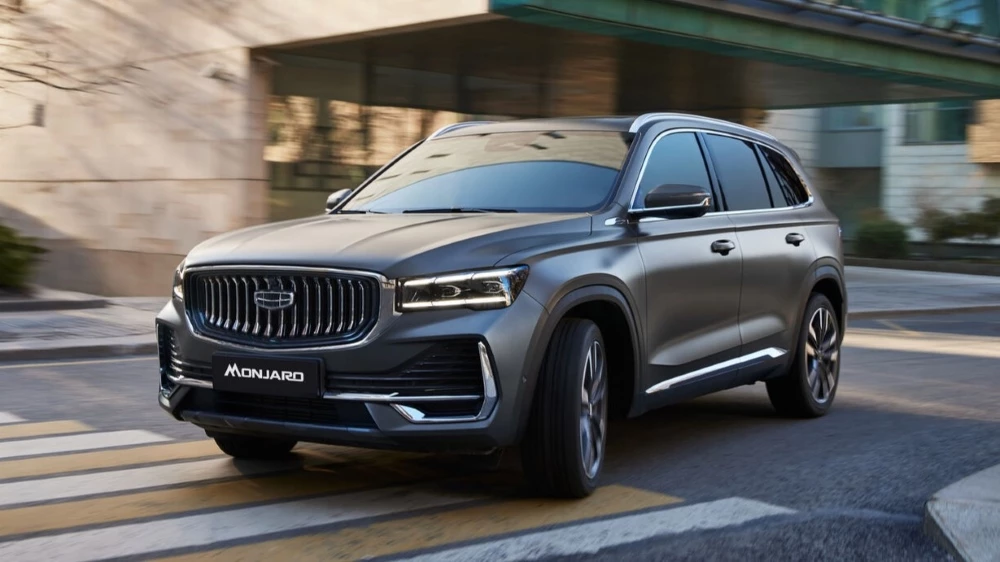 Обновленный кроссовер Geely Monjaro модельного года в России сбоку спереди в динамике новый цвет Lomo Grey